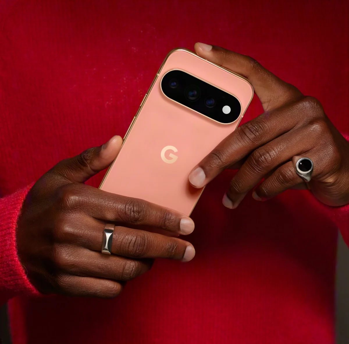 Two hands holding a coral Pixel against a red sweater