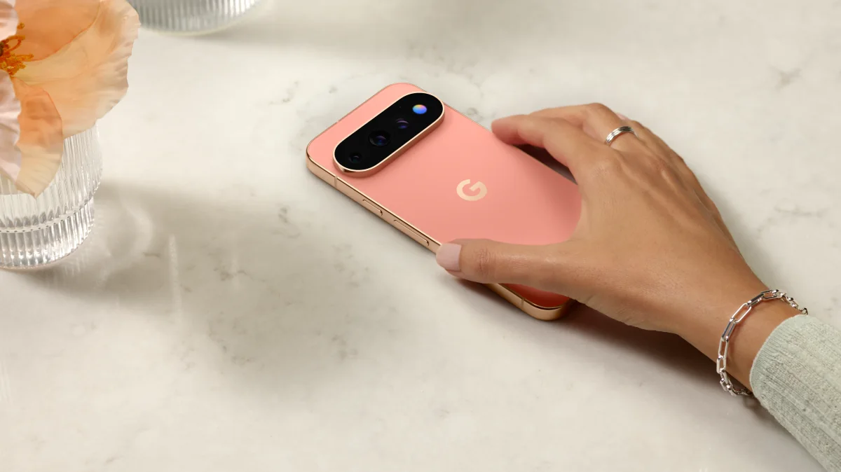 A coral Pixel resting on a marble table under a hand